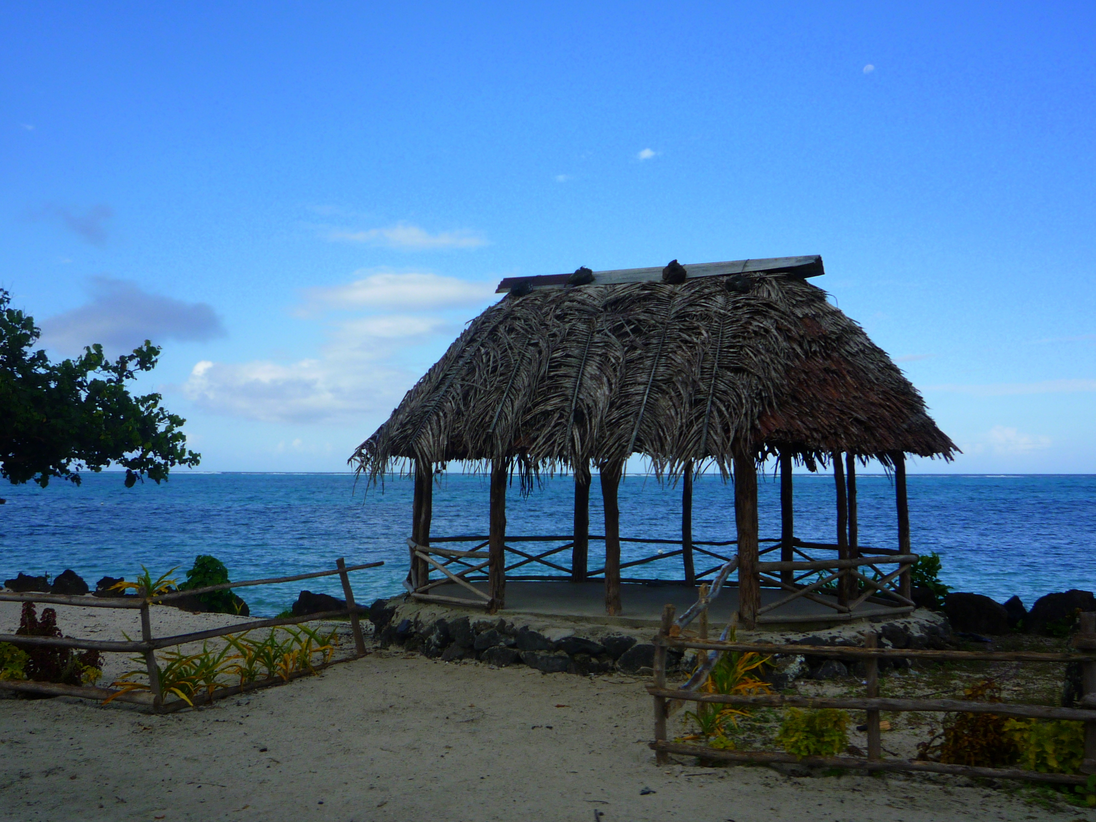 An open-sided Samoan beach fale beside palm trees and the sea